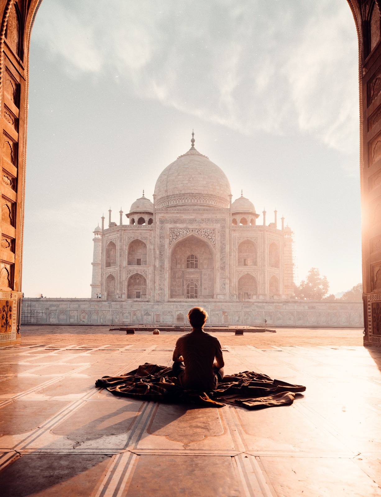A person sitting in meditation facing the Taj Mahal through a mosque archway in golden morning light